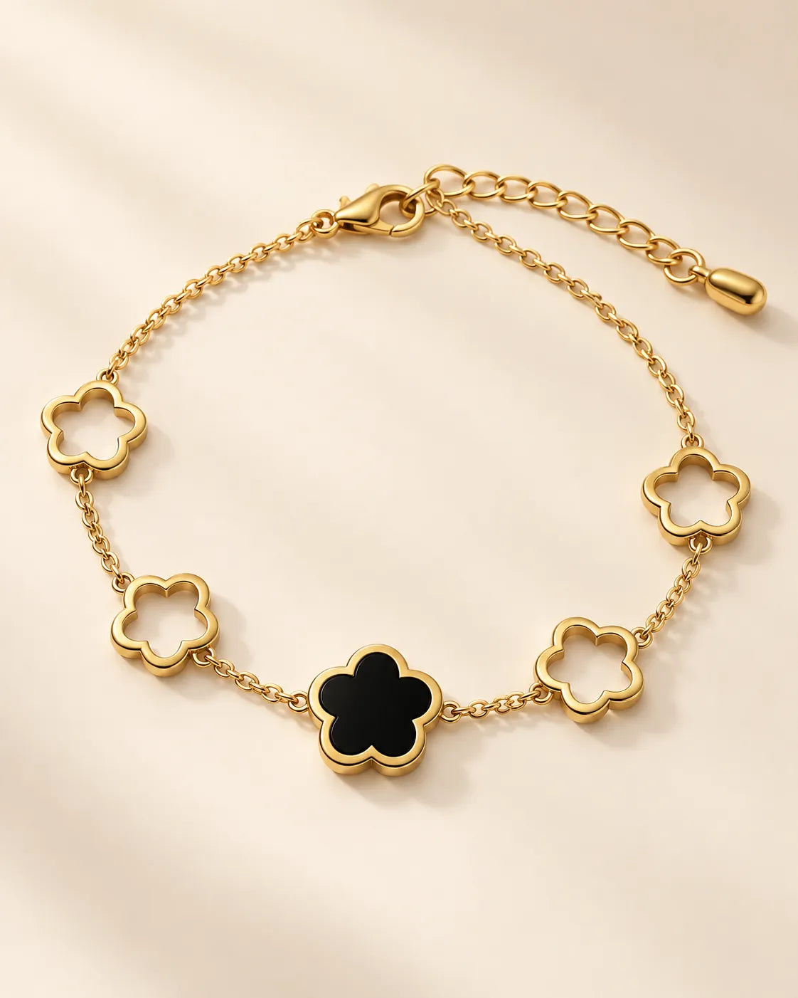 Black clover flower gold bracelet laid in a curve on cream