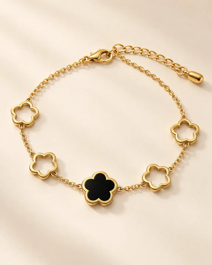 Black clover flower gold bracelet laid in a curve on cream