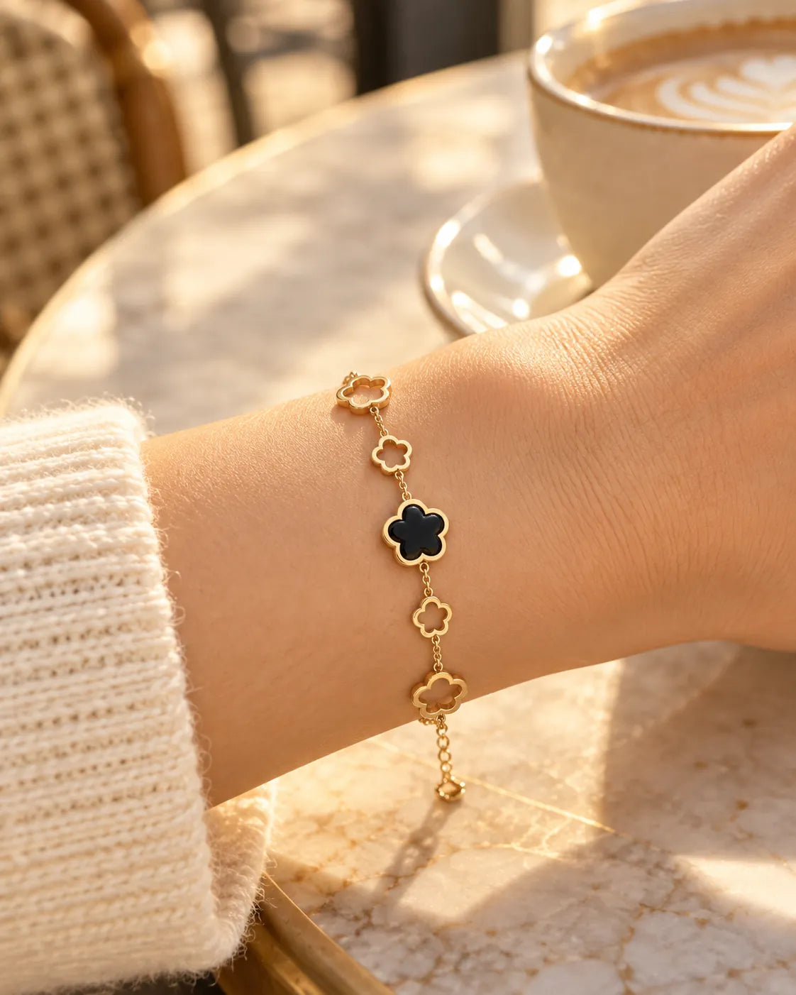 Wrist in a cream knit at a cafe wearing the black clover bracelet