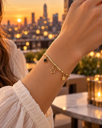 Wrist wearing the gold star charm bracelet against a city skyline at sunset