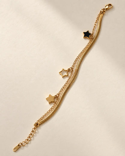 Gold layered bracelet with black enamel and gold star charms on cream