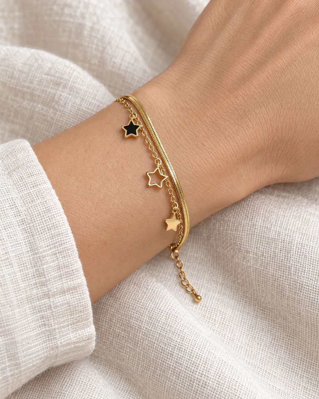 Wrist in a white knit wearing the gold and black star charm bracelet