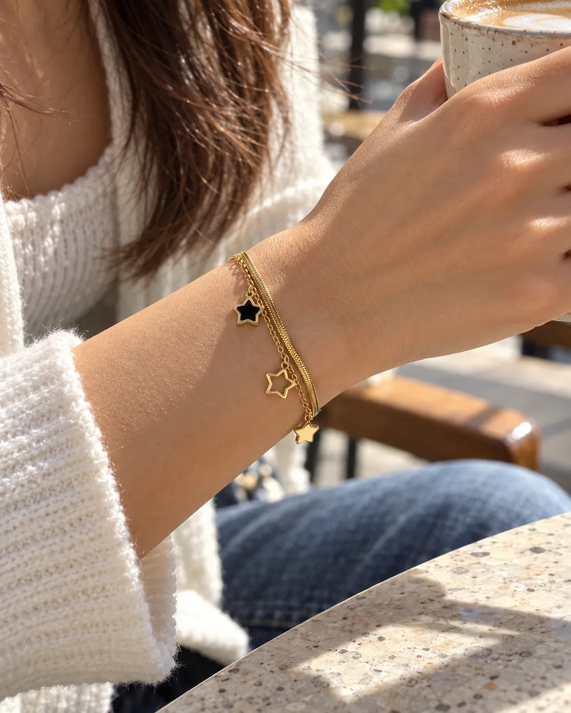 Wrist at a cafe with denim wearing the layered star charm bracelet