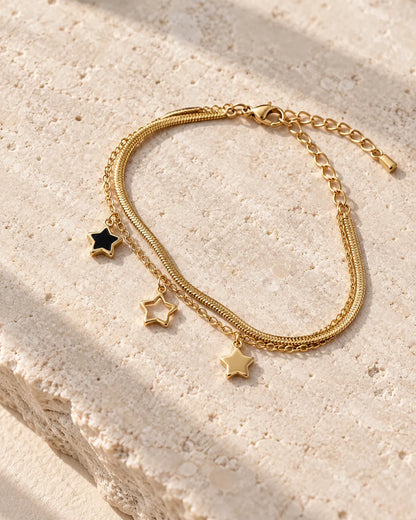 Gold and black star charm bracelet on a stone surface