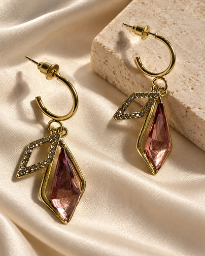 Pink crystal geometric drop earrings on satin beside a stone block