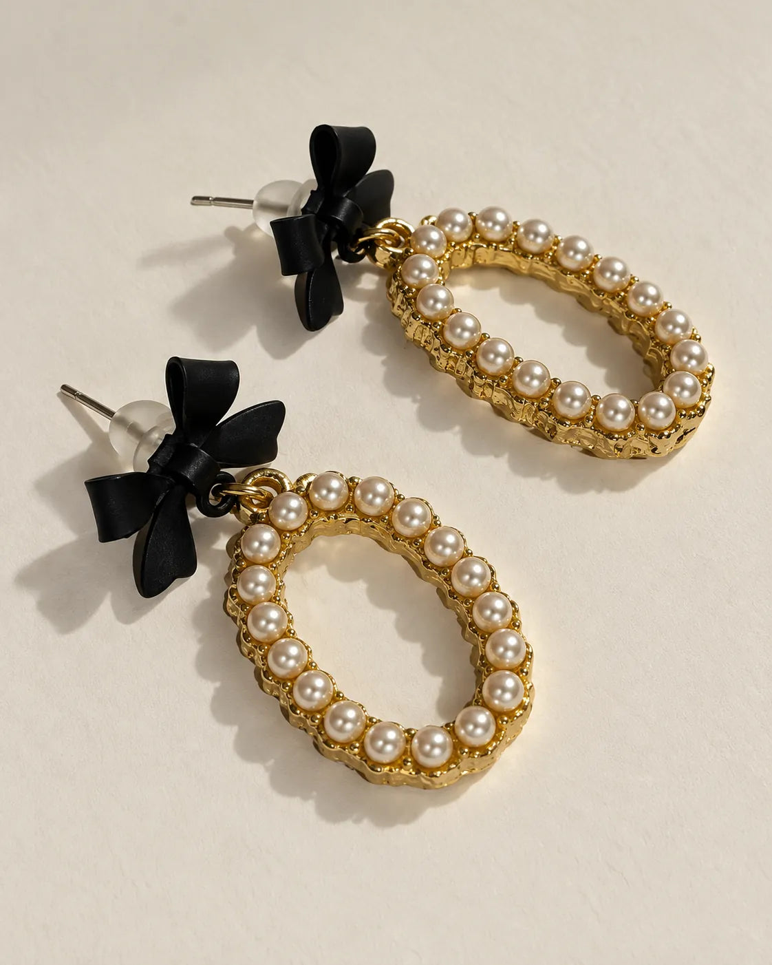 Black bow oval drop earrings laid at an angle showing the stud posts