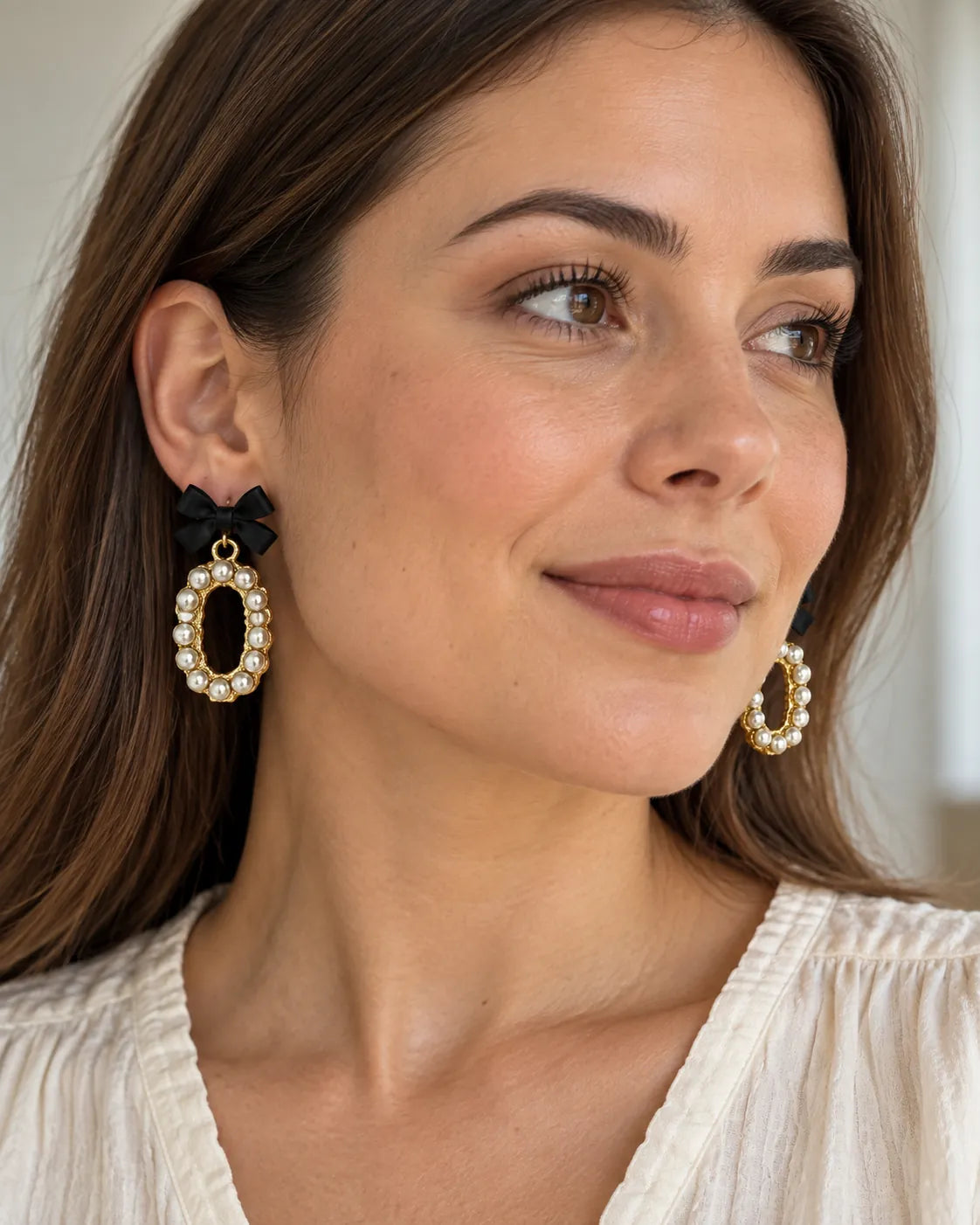 Model in a cream top wearing the black bow pearl-look oval earrings