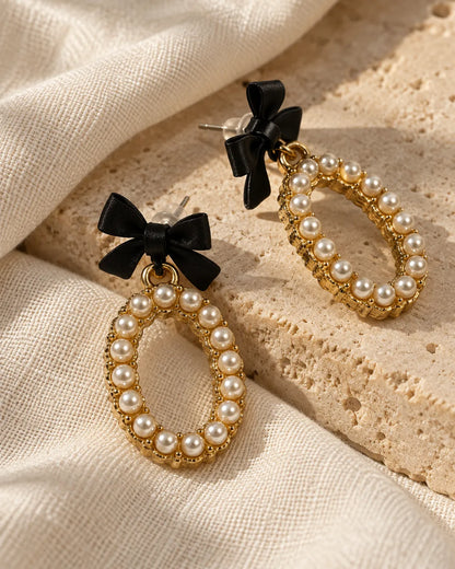 Black bow pearl-look oval earrings resting on stone and cream fabric