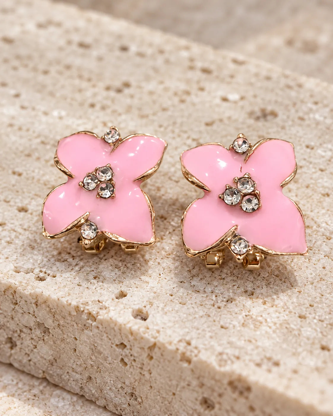 Pink enamel camellia flower studs resting on stone