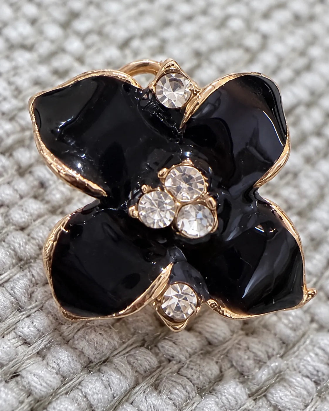 Close-up of a black camellia stud on grey knit showing crystals and gold-tone rim