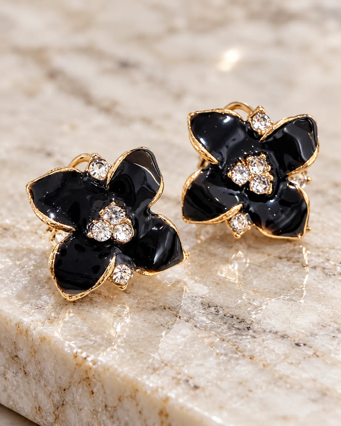 Black enamel camellia flower studs resting on marble