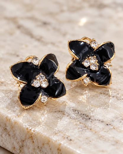 Black enamel camellia flower studs resting on marble