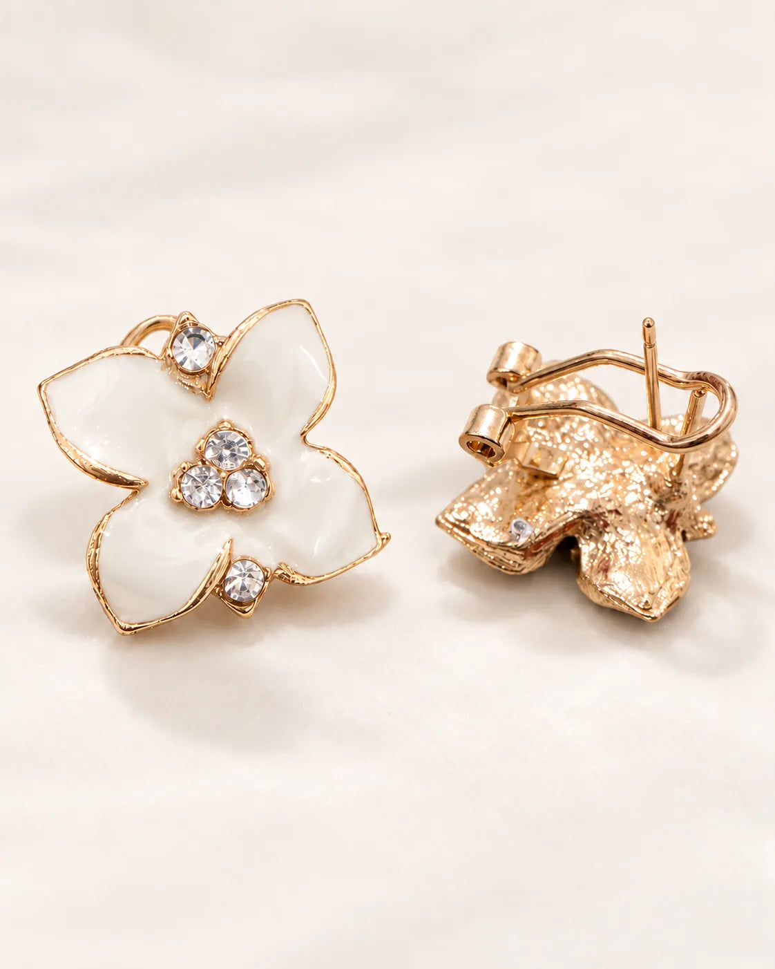 White enamel camellia stud front beside its gold-tone clip-style back on cream