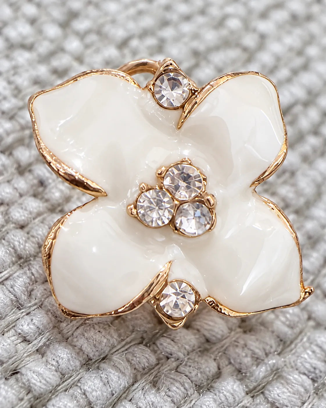 Close-up of a white enamel camellia stud with crystal centre on grey knit