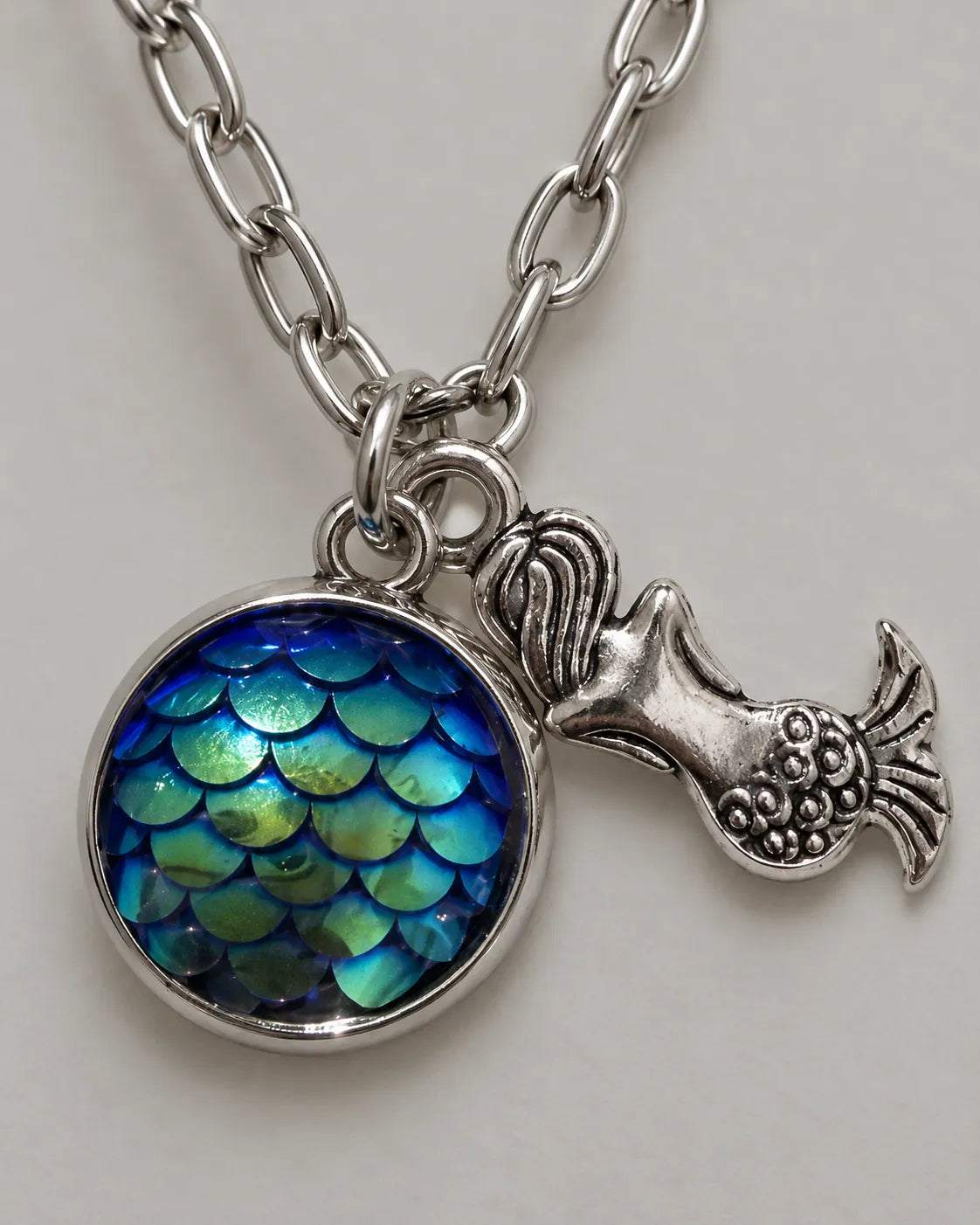 Close-up of the iridescent blue-green scale cabochon and mermaid charm