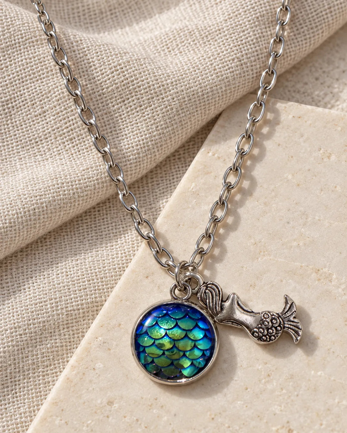Silver-tone mermaid charm necklace resting on cream linen