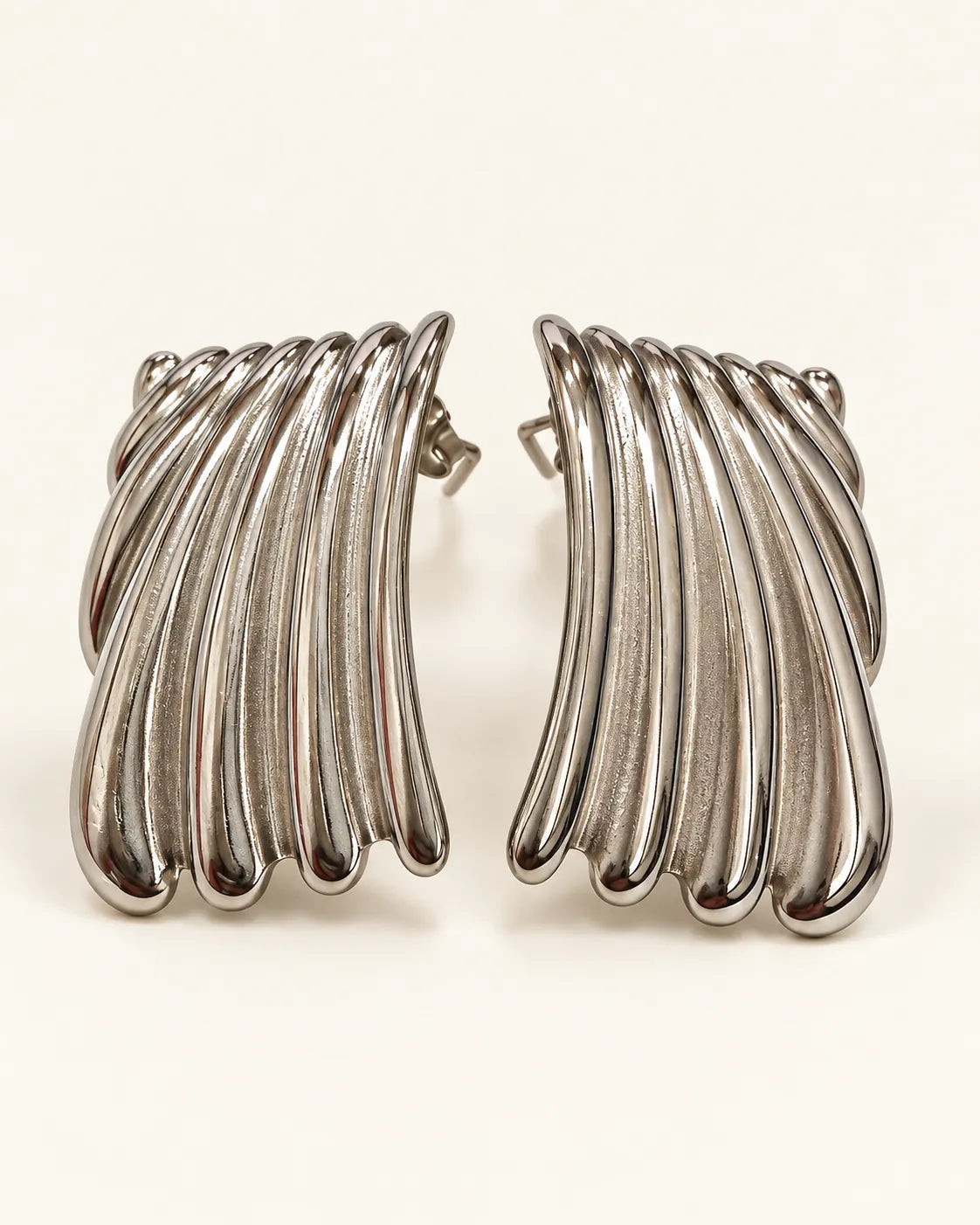 Pair of silver ribbed wave stud earrings on a cream background