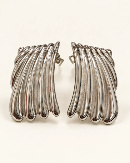 Pair of silver ribbed wave stud earrings on a cream background
