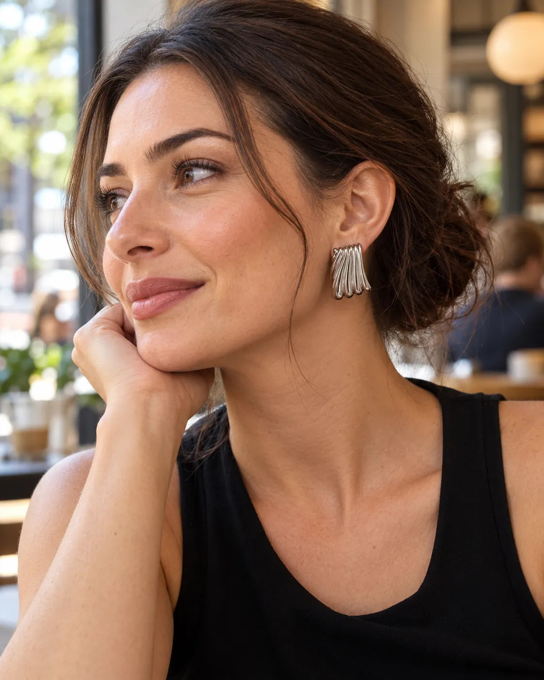 Model at a café in a black top wearing the silver ribbed studs