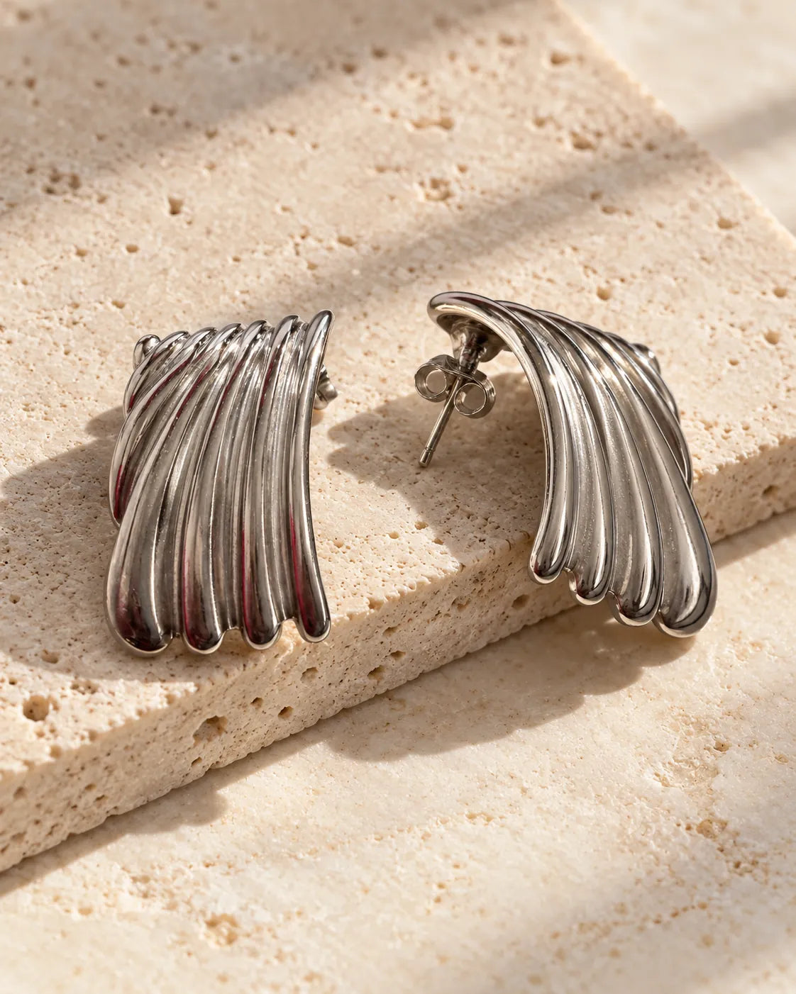 Silver ribbed stud earrings resting on a stone surface