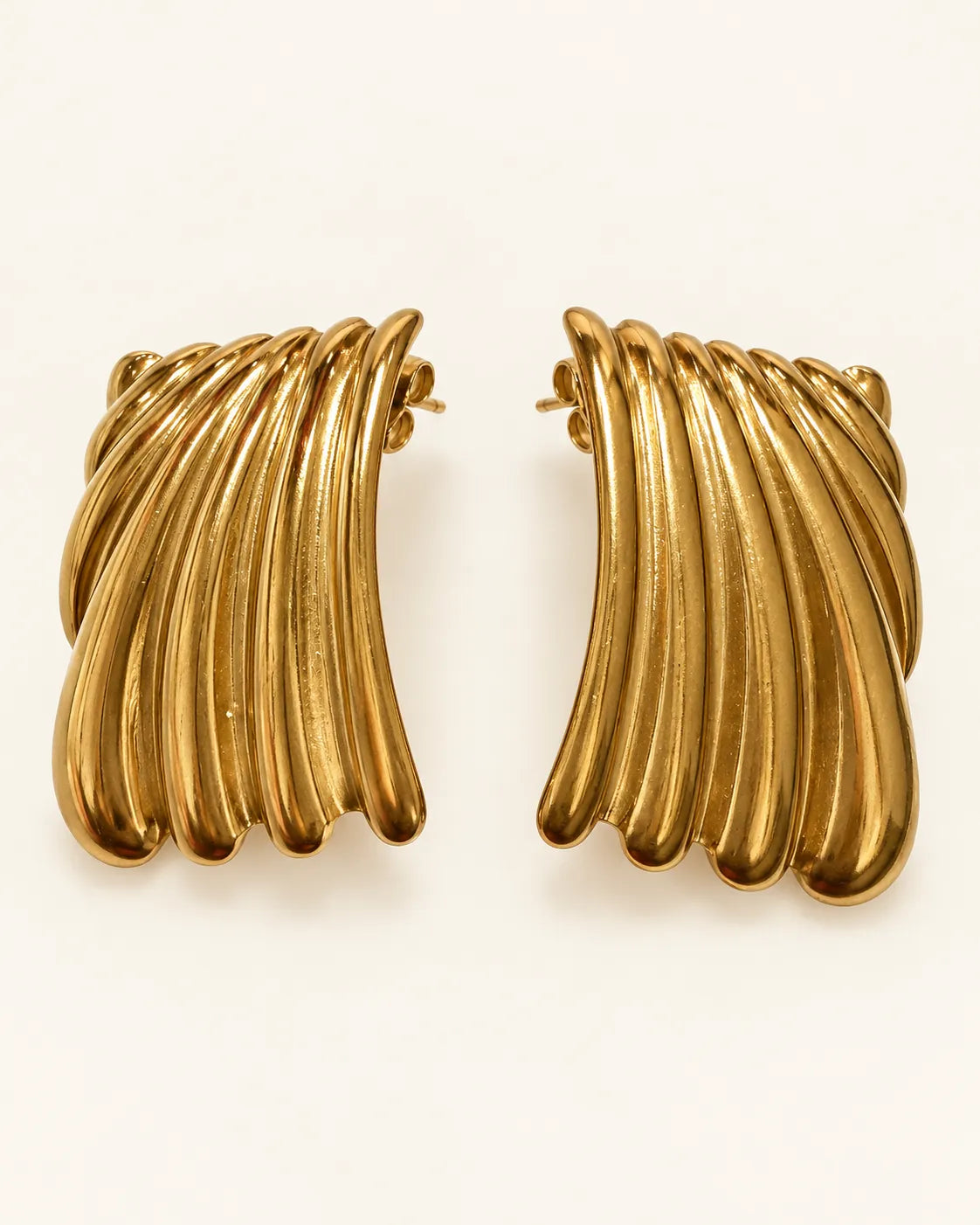 Pair of gold ribbed wave stud earrings on a cream background