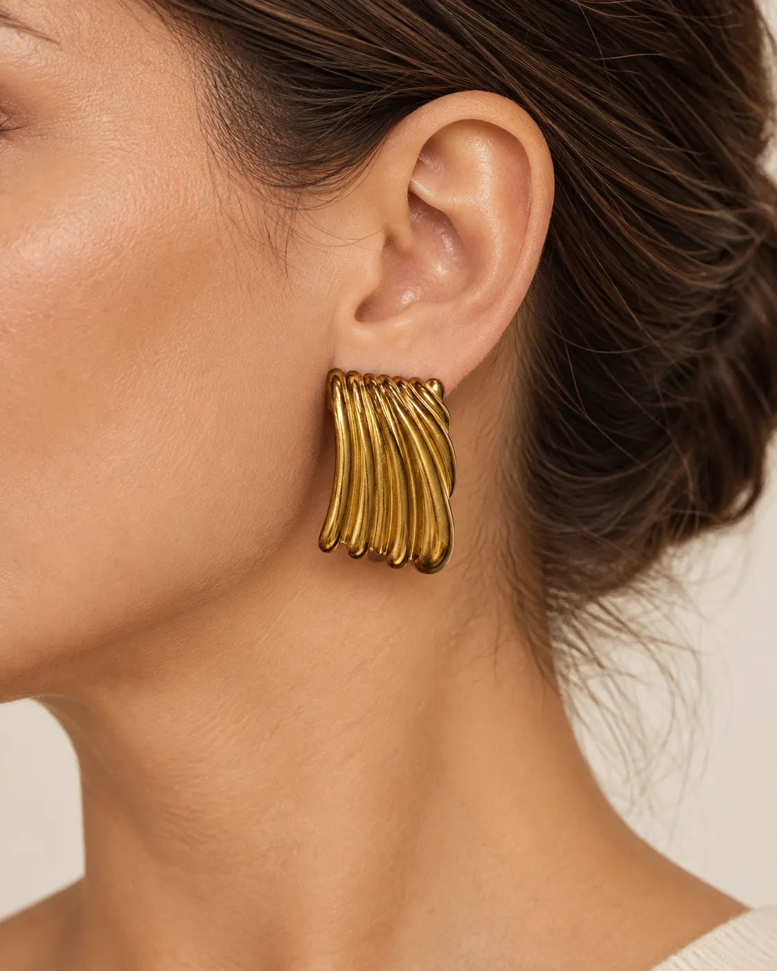 Close-up of a gold ribbed stud earring worn on the ear