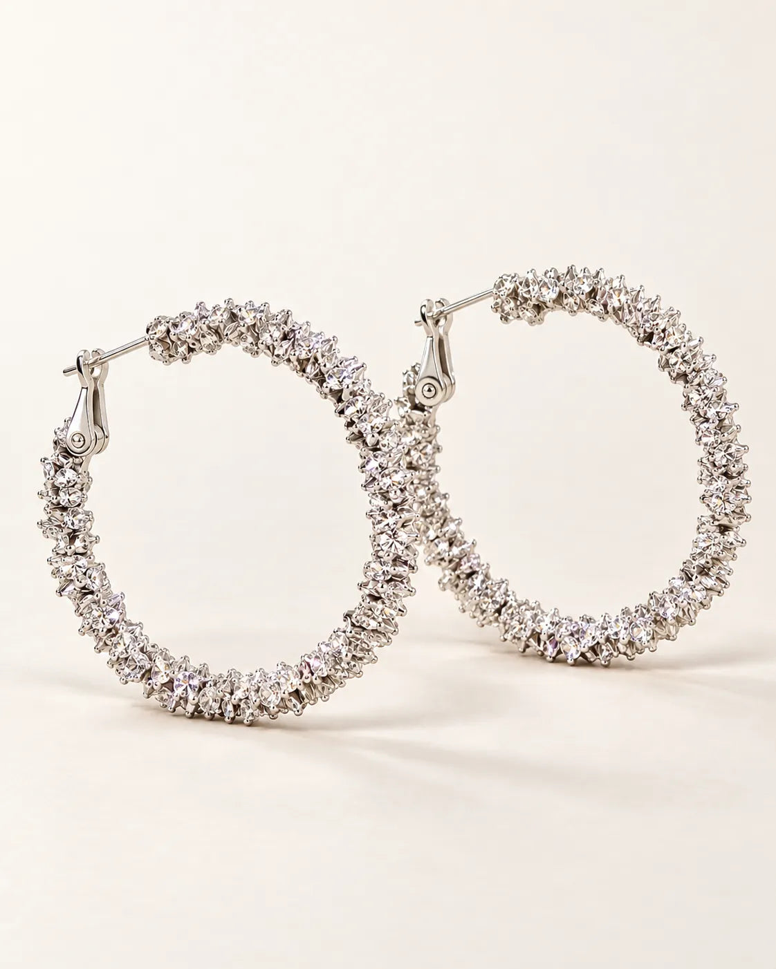 Pair of large silver crystal cluster hoop earrings on a cream background
