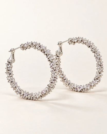 Pair of large silver crystal cluster hoop earrings on a cream background
