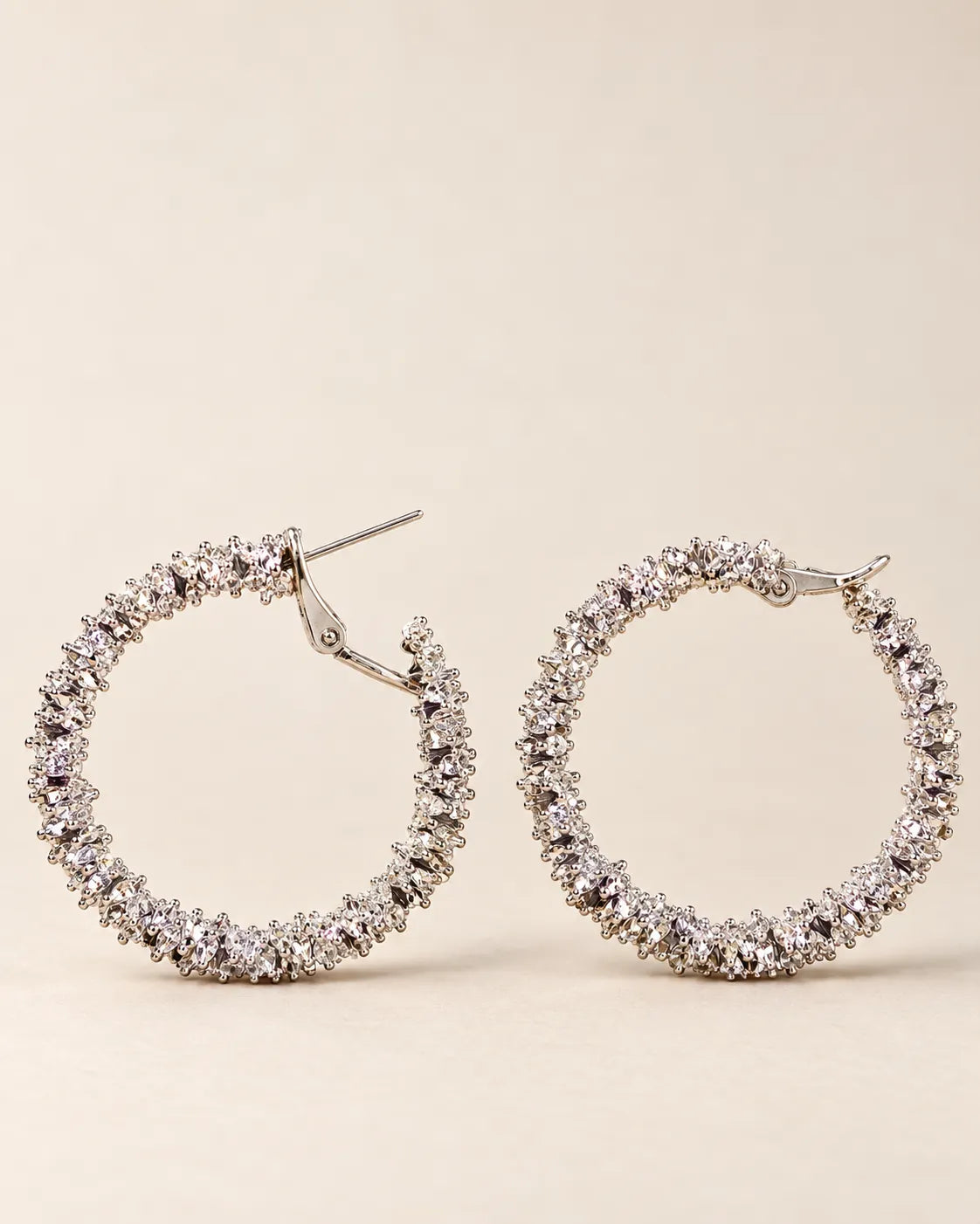 Silver crystal cluster hoops laid side by side on cream