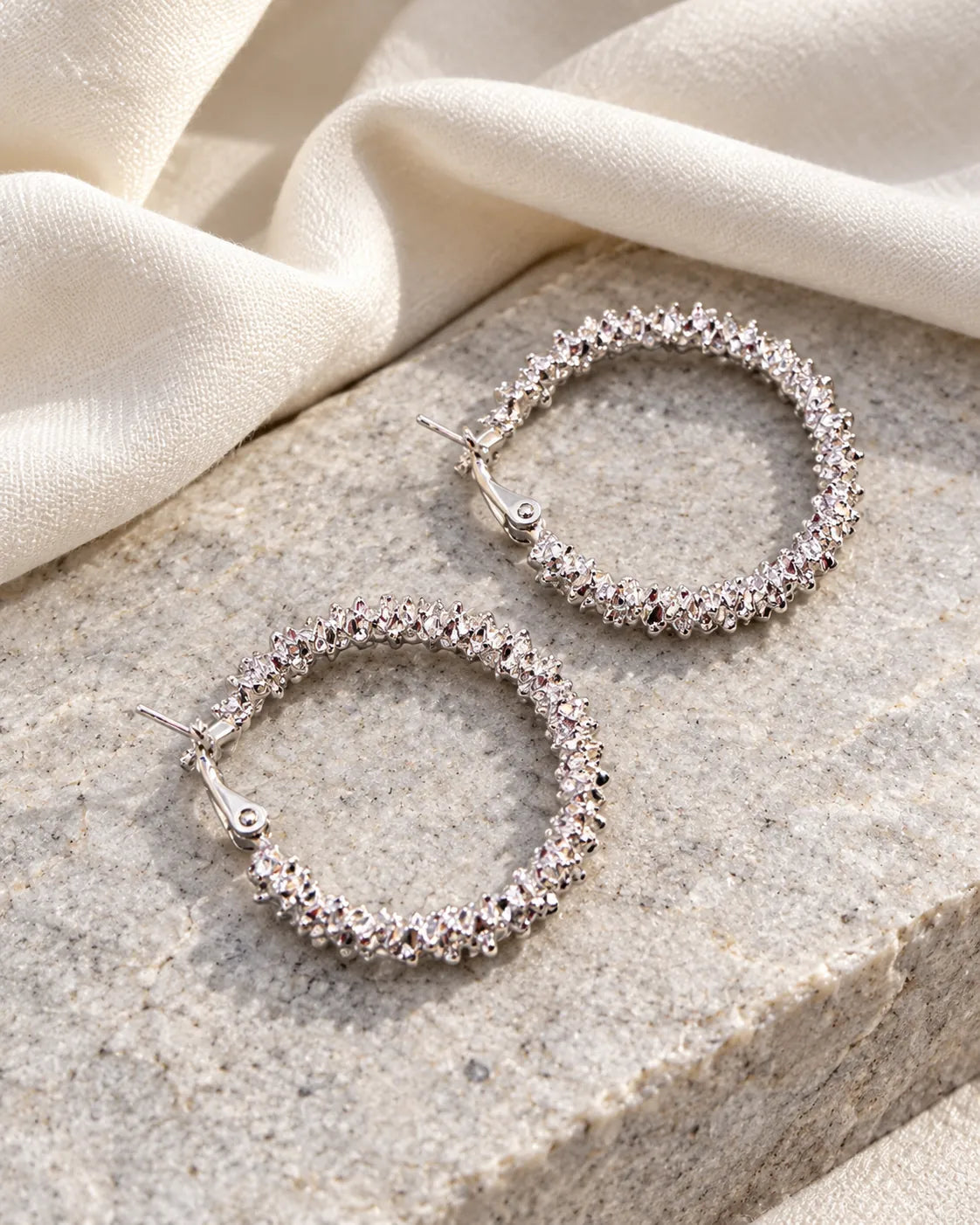 Silver crystal cluster hoop earrings on a stone block with linen