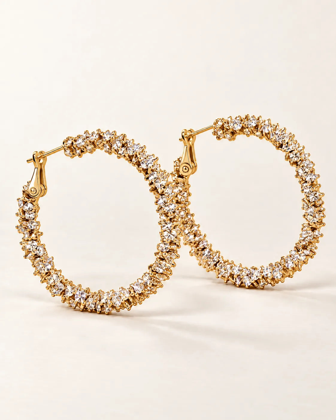 Pair of large gold crystal cluster hoop earrings on a cream background