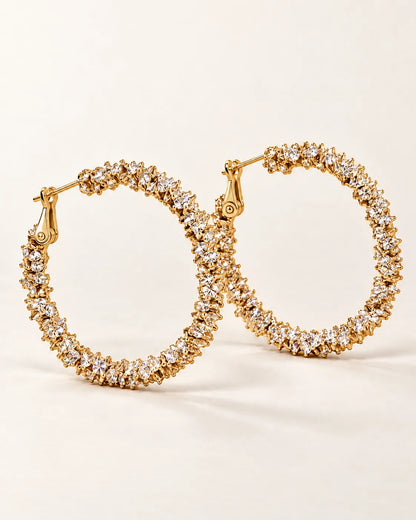 Pair of large gold crystal cluster hoop earrings on a cream background