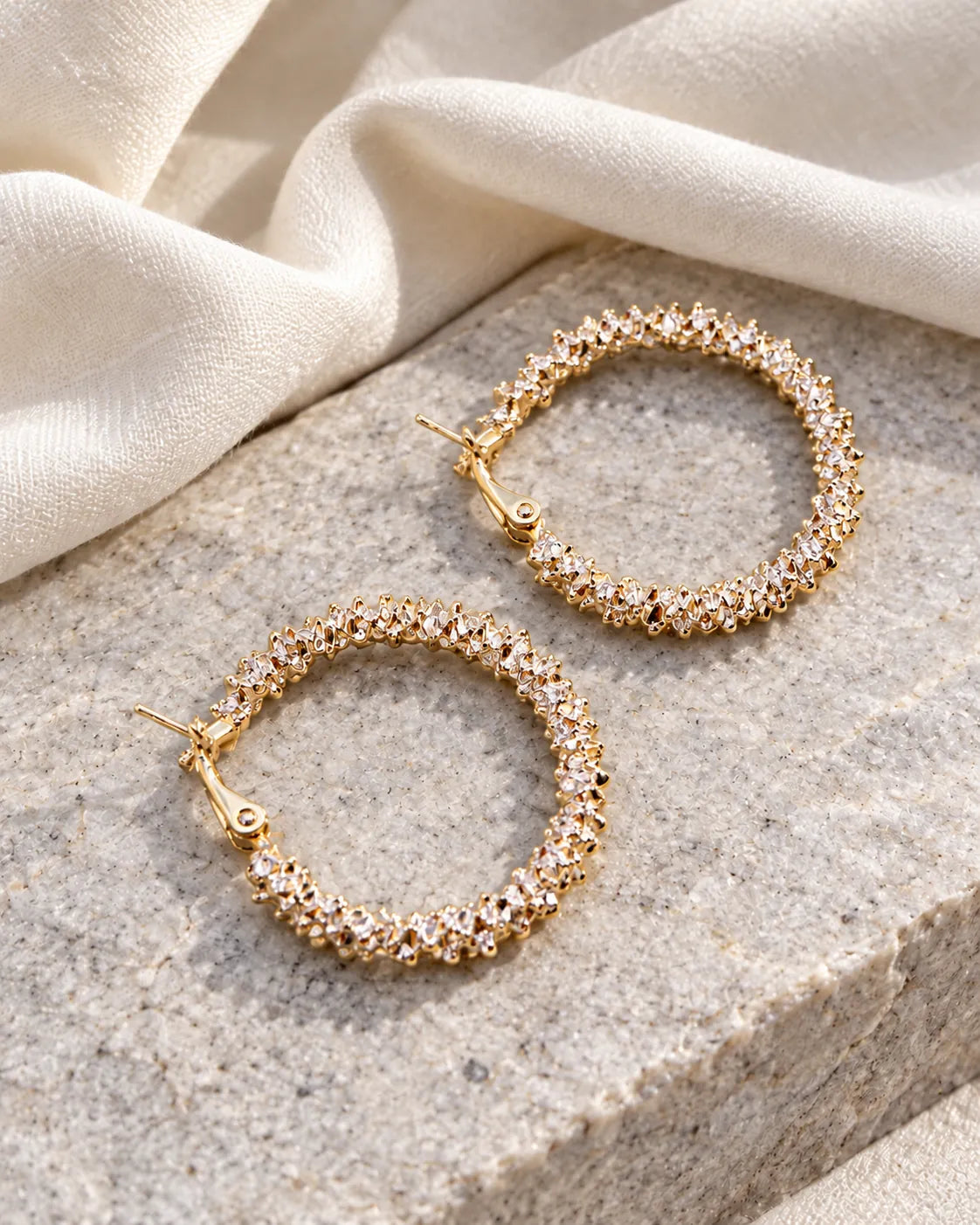Gold crystal cluster hoop earrings on a stone block with linen