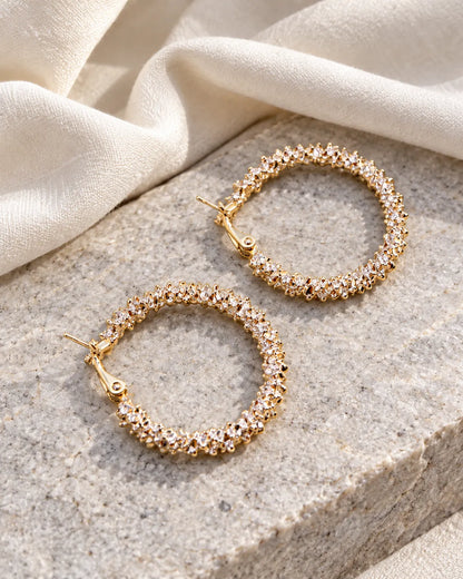 Gold crystal cluster hoop earrings on a stone block with linen