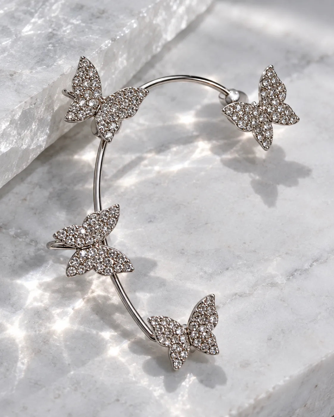 Silver butterfly ear cuff laid on a sparkling marble surface