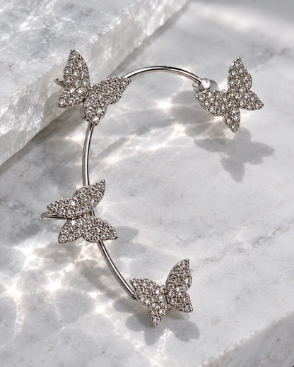 Silver butterfly ear cuff laid on a sparkling marble surface