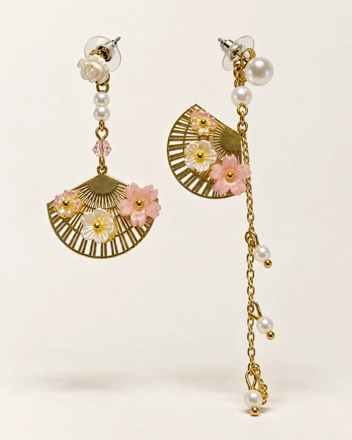 Asymmetric gold fan and pearl-look chain dangle earrings on a cream background