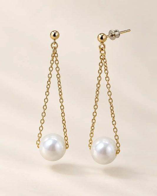Gold pearl long chain drop earrings on a cream background