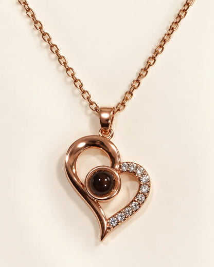 Rose gold heart pendant with a dark centre stone on a cream background