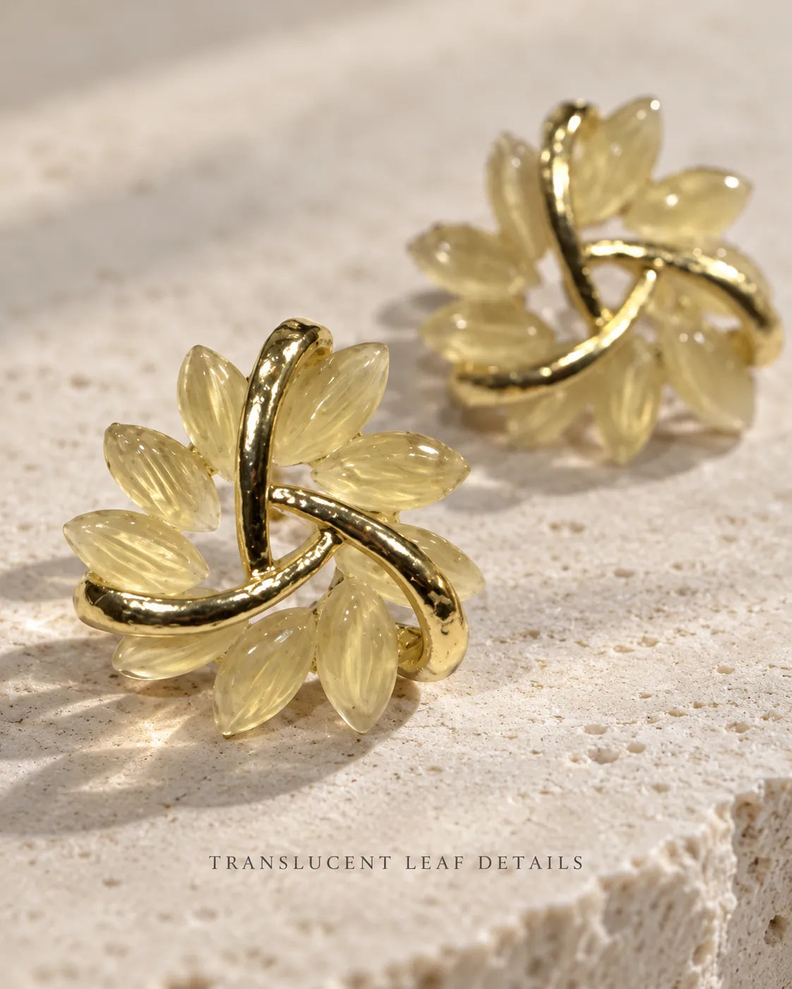 Gold swirl flower studs with pale opal petals on a stone surface