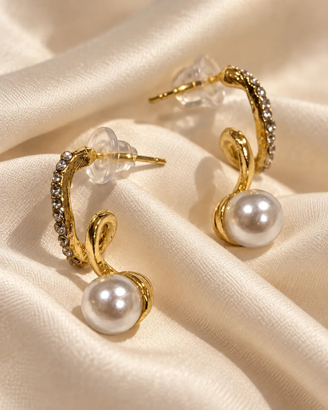 Pair of gold twisted pearl-look stud earrings with rhinestones on draped satin