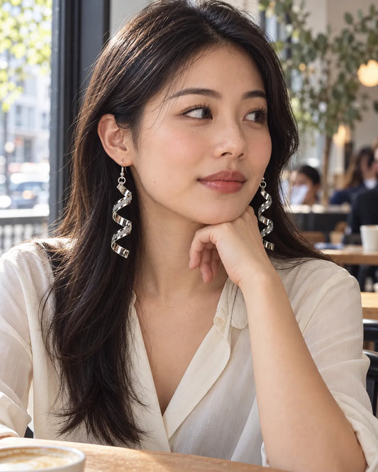 Model at a café in a cream blouse wearing the silver spiral earrings