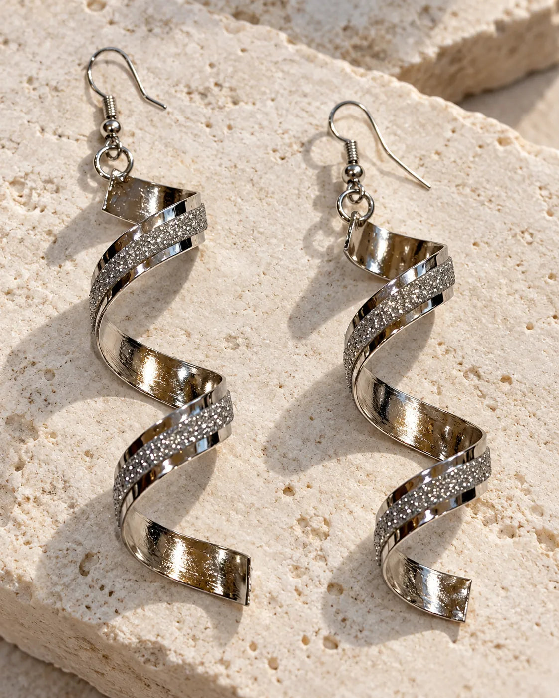 Silver spiral statement earrings resting on a stone block