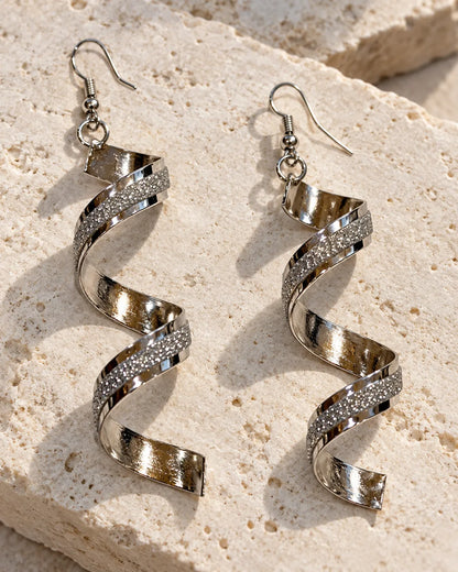 Silver spiral statement earrings resting on a stone block