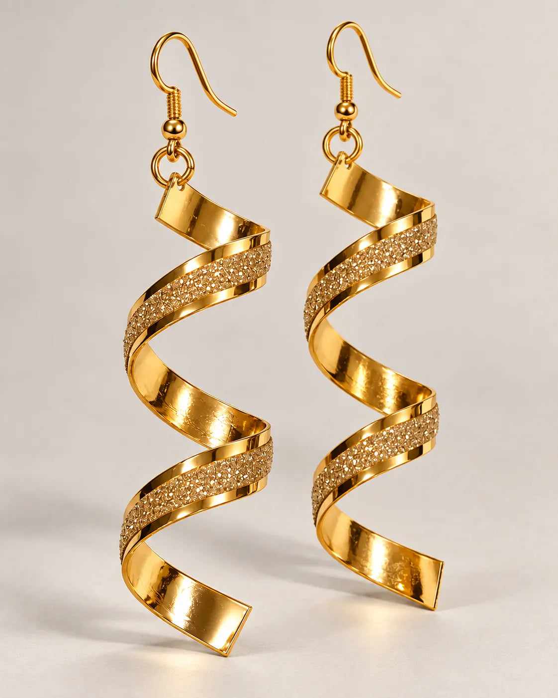Gold-tone spiral frosted drop earrings hanging on a pale background