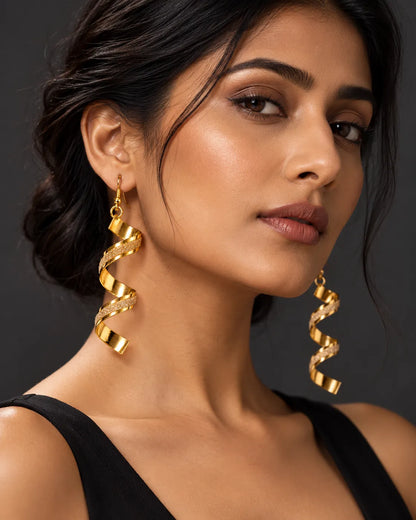 Model with a sleek bun wearing the gold spiral earrings against a dark backdrop