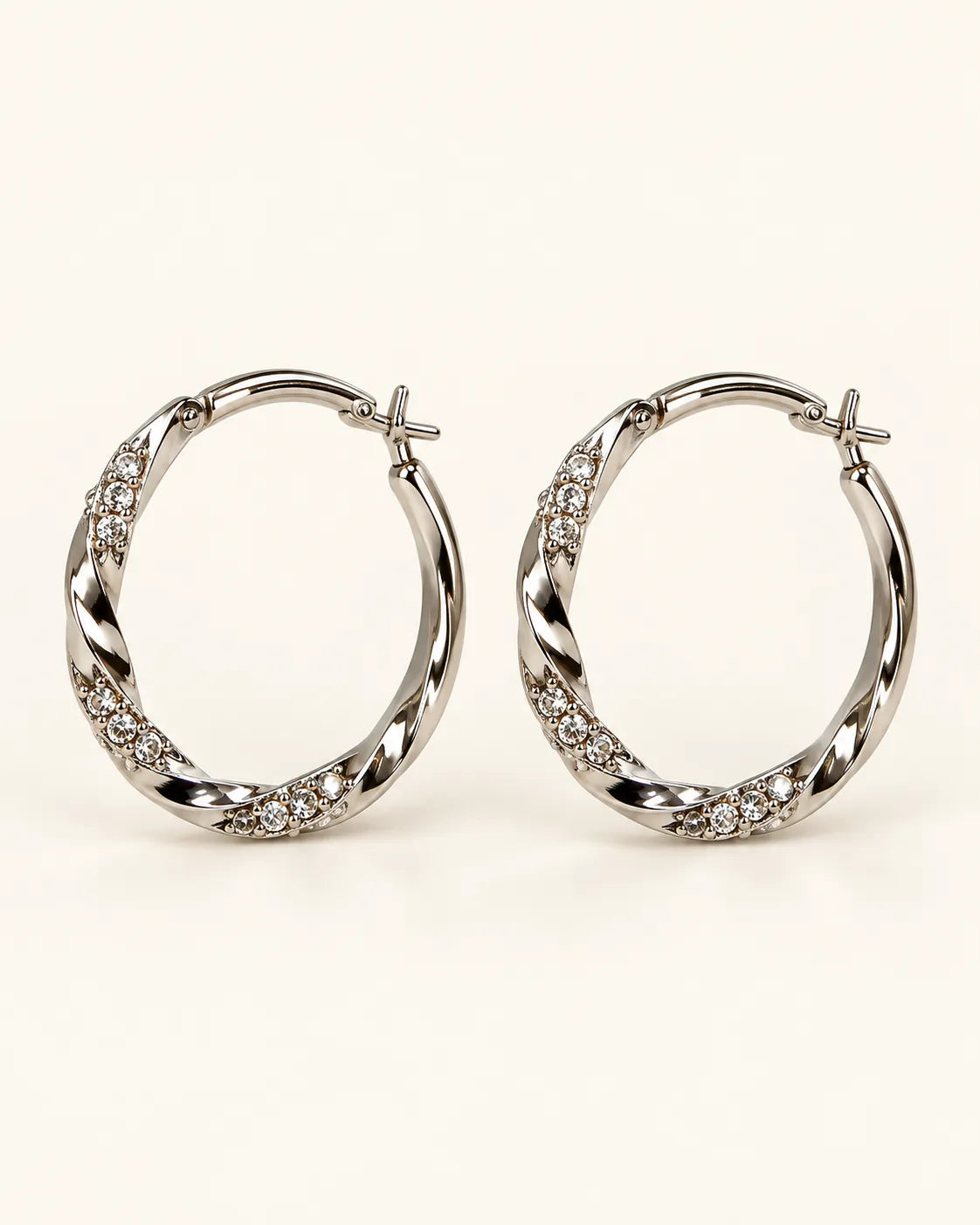 Pair of silver twisted hoop earrings with rhinestone sections on a cream background
