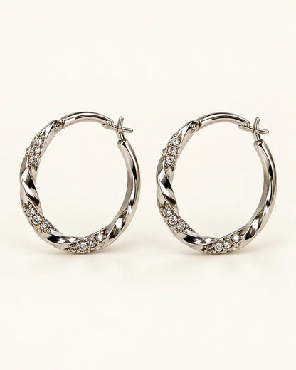 Pair of silver twisted hoop earrings with rhinestone sections on a cream background