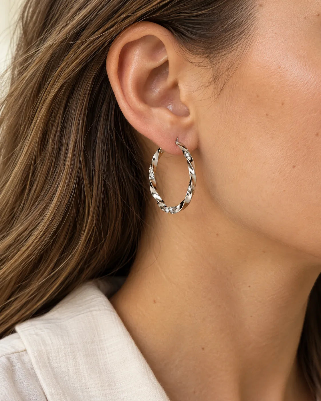 Close-up of a silver twisted rhinestone hoop worn on the ear