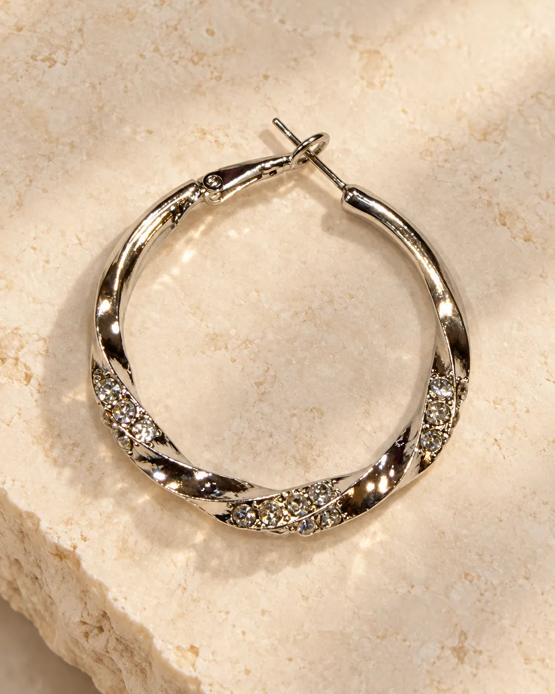 Single silver rhinestone twisted hoop resting on a stone surface